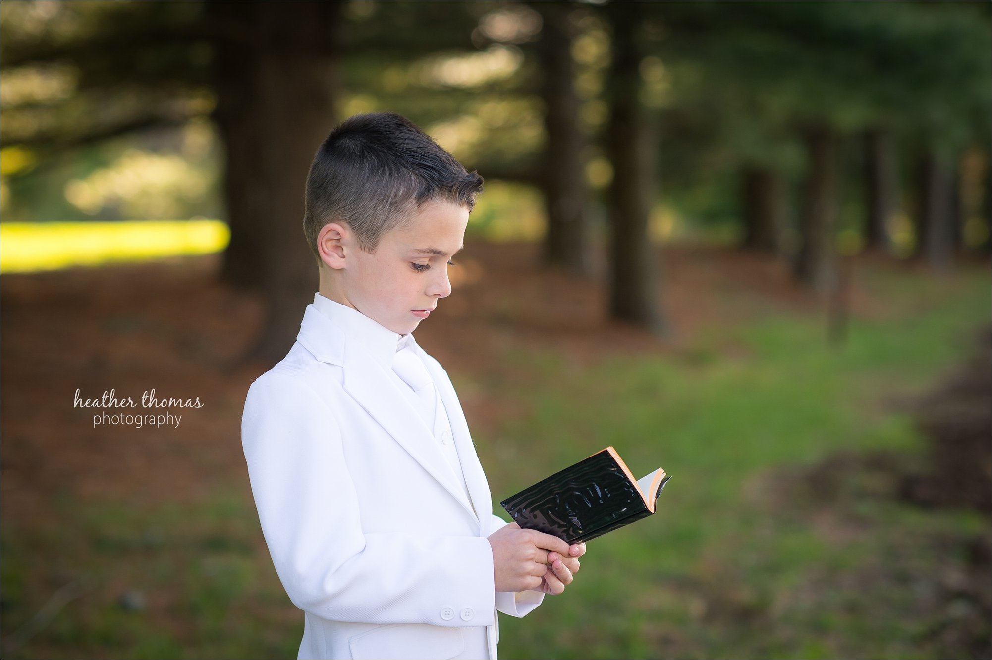 Newtown pa communion photography-39.jpg a 2nd grade boy reading his bible outside the catholic church in newtown pa