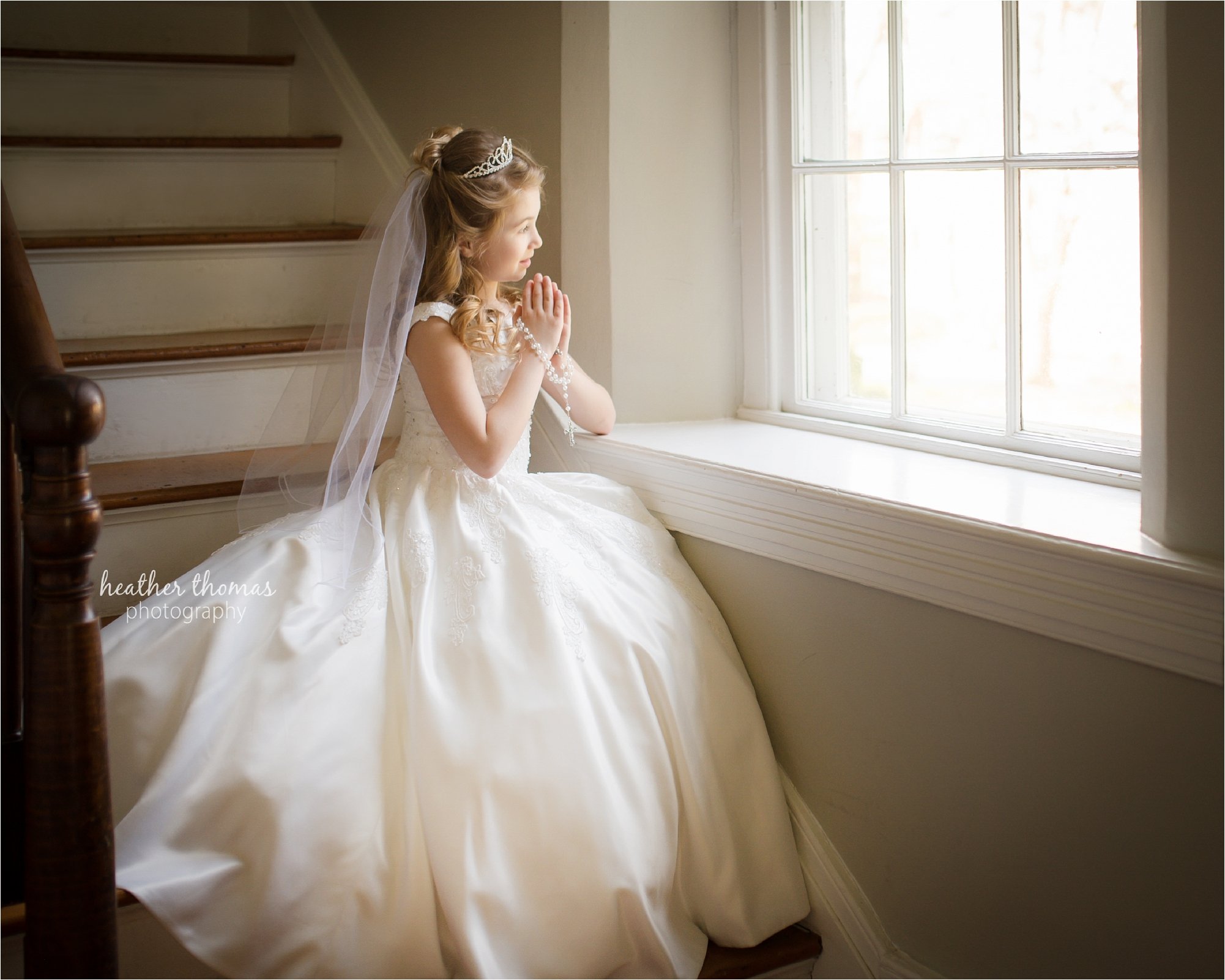 a girl in a communion dress looking out the window at the photography studio in newtown maternity portraits of a family of three at azalea garden waterworks with heather thomas photography