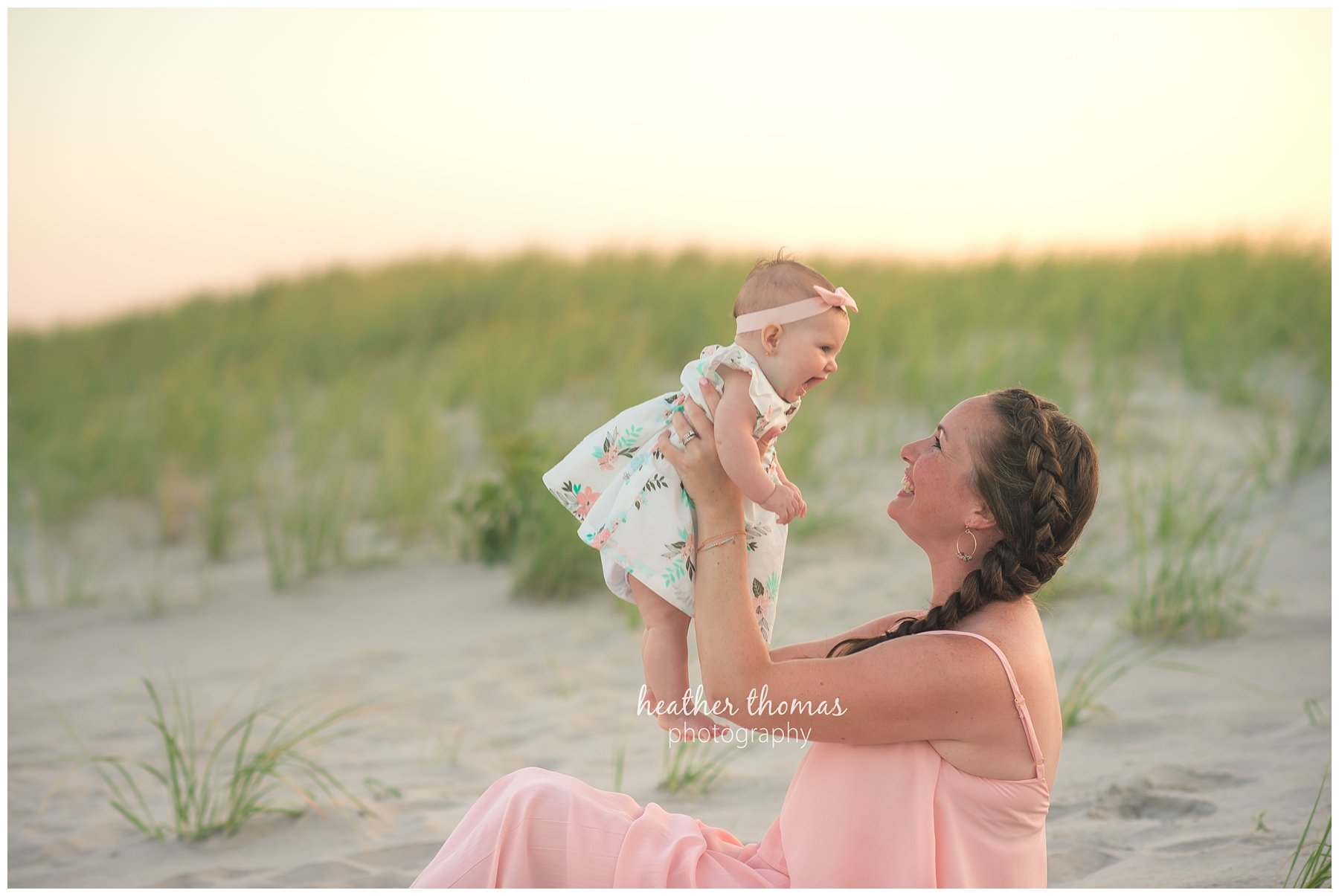 family beach photography ocnj-14.jpg a mother wearing pink lifting her 5 month old daughter up on the beach in ocean city nj