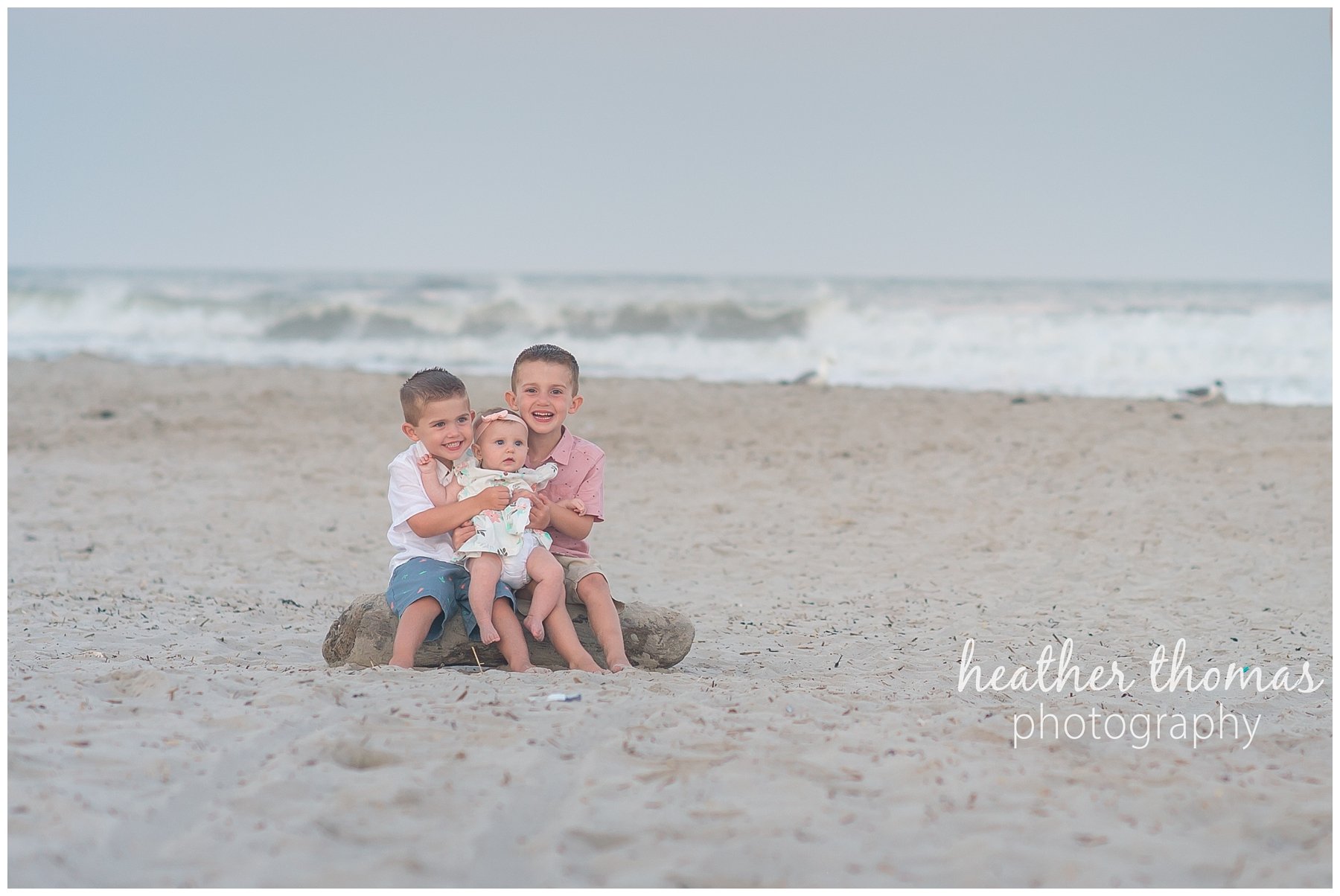 family beach photography ocnj-51.jpg three children sitting on a piece of driftwood on the beach in ocnj
