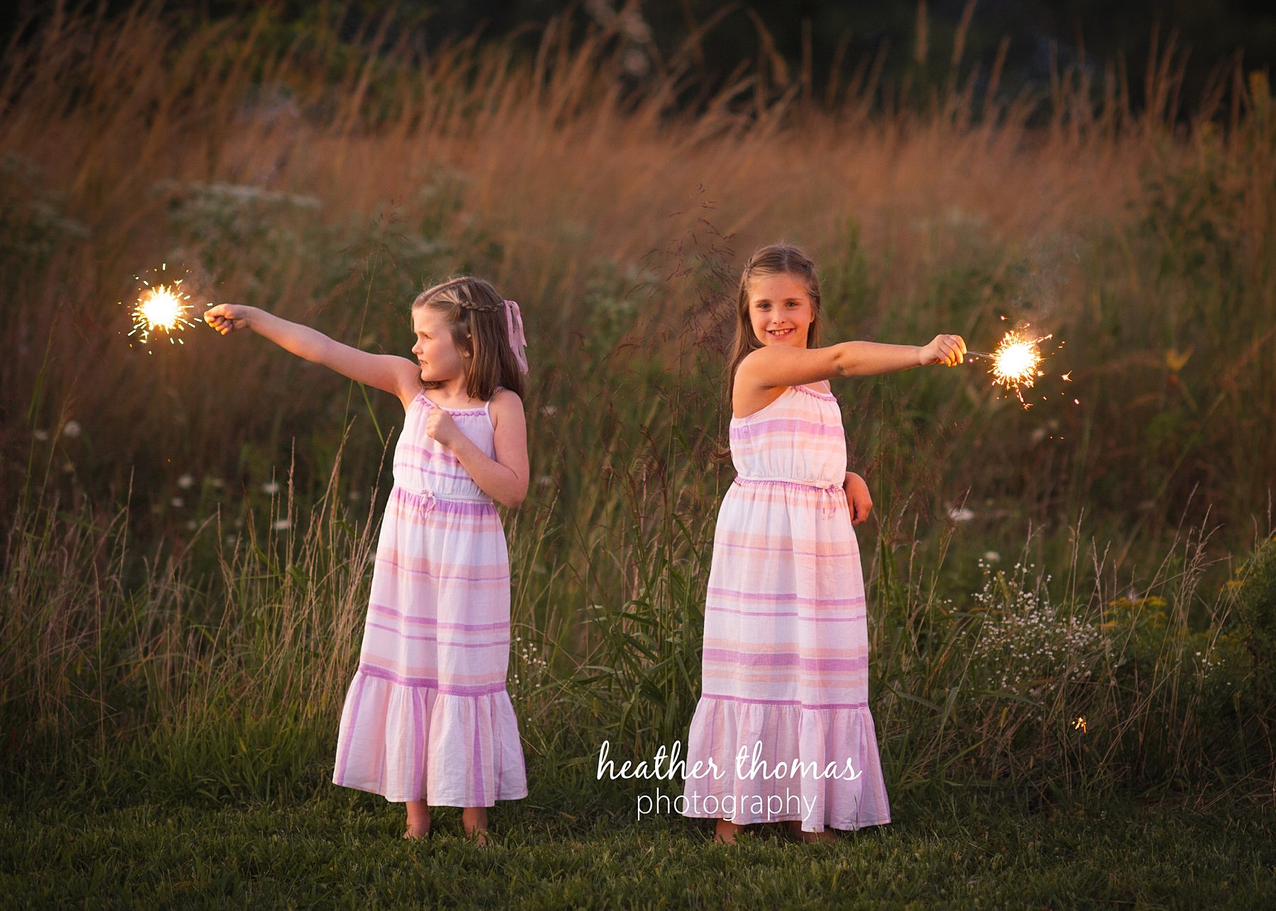 field family portraits in philadelphia a picture of sisters outside at a field with fireworks in Philadelphia with heather thomas photography