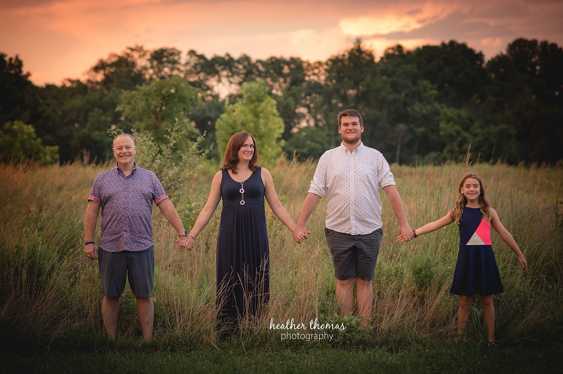 field family portraits in philadelphia a picture of a family holding hands outside in a field in philadelphia with heather thomas photography