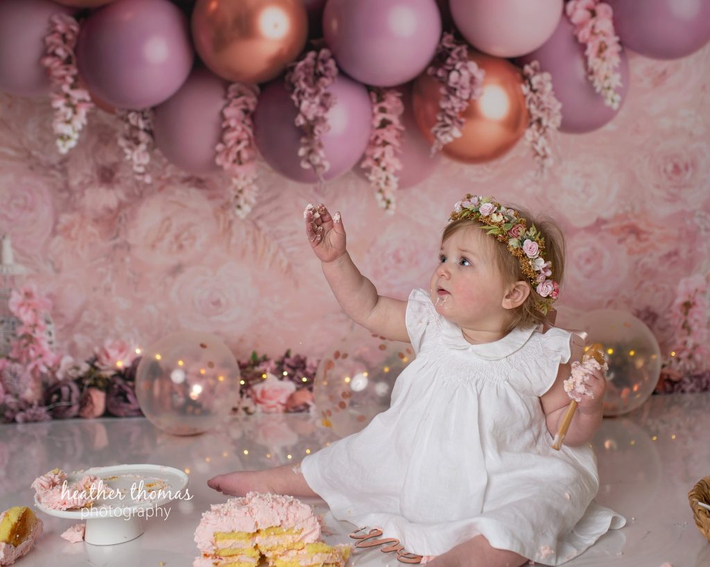 5 Things To#15 Ask Before Your Cake Smash Shoot | Bucks County Family Photographer little one plays with frosting under balloons by Heather Thomas Photography